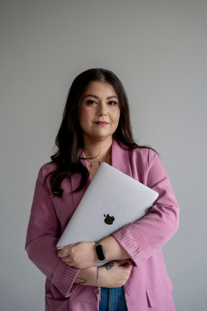 Kobieta pozująca w różowym żakiecie z laptopem